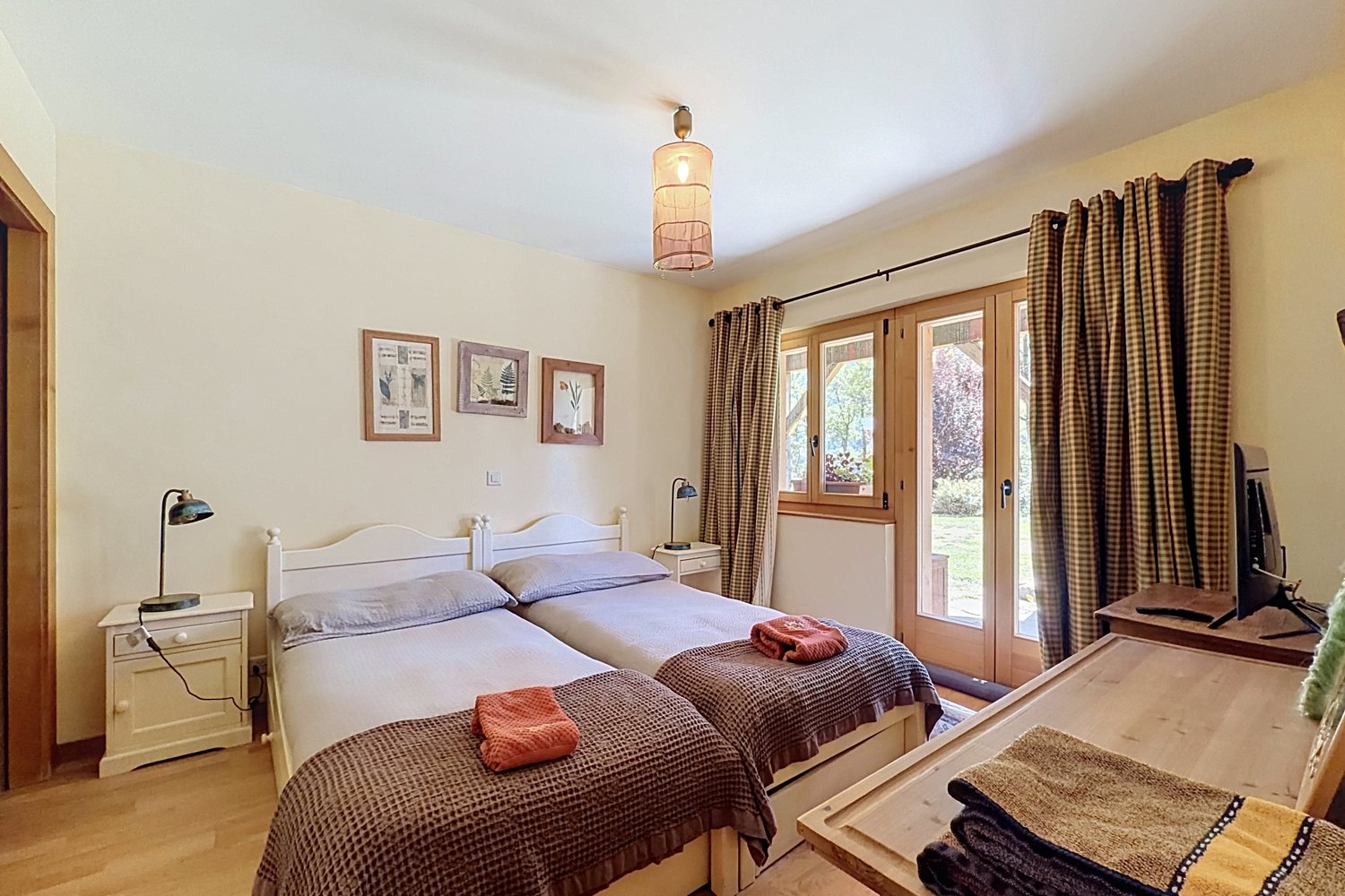 Chambre d'amis avec deux lits et porte-fenêtre ouvrant sur le jardin.