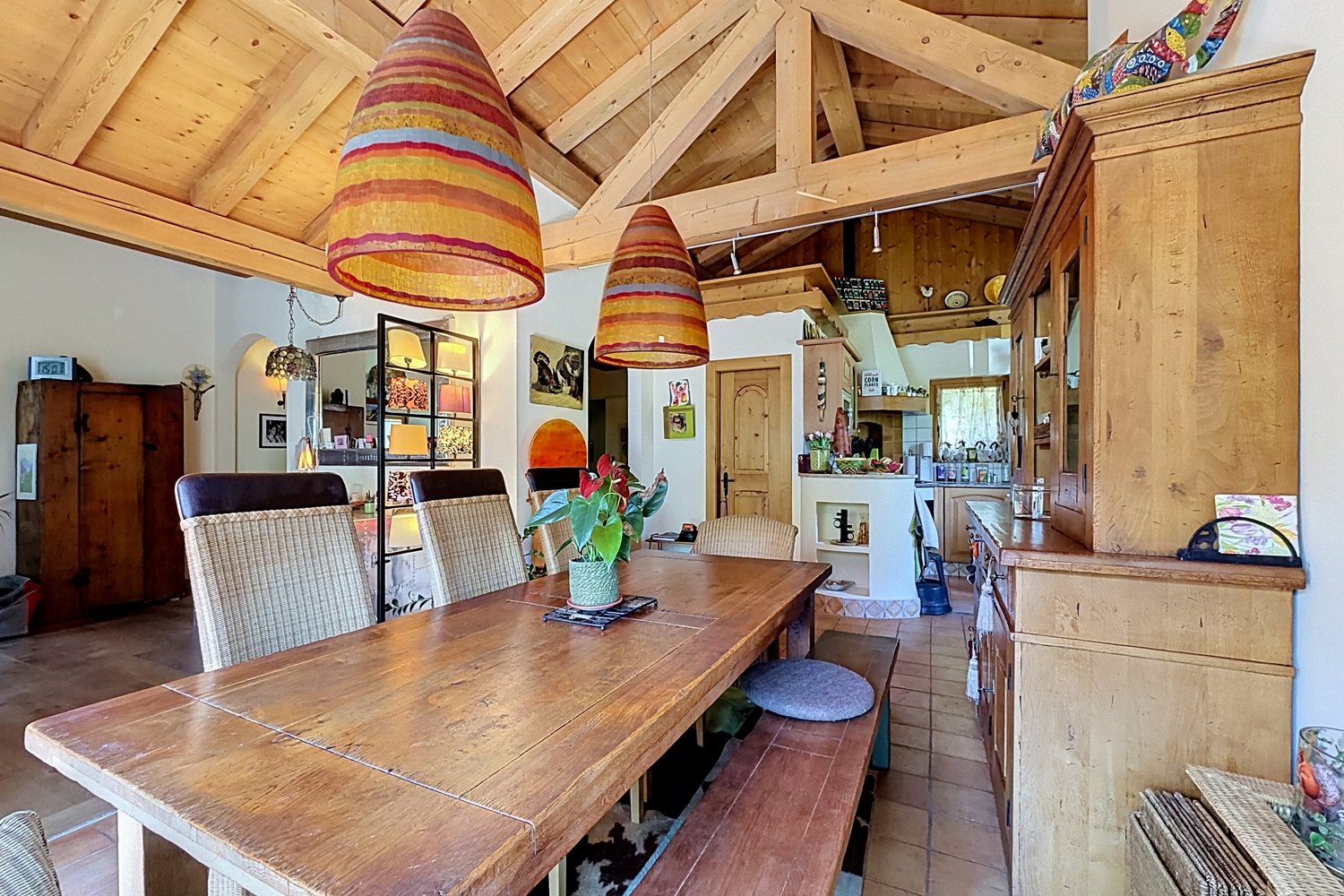 Grande table de bois sous des suspensions tressées, cuisine ouverte en arrière-plan.