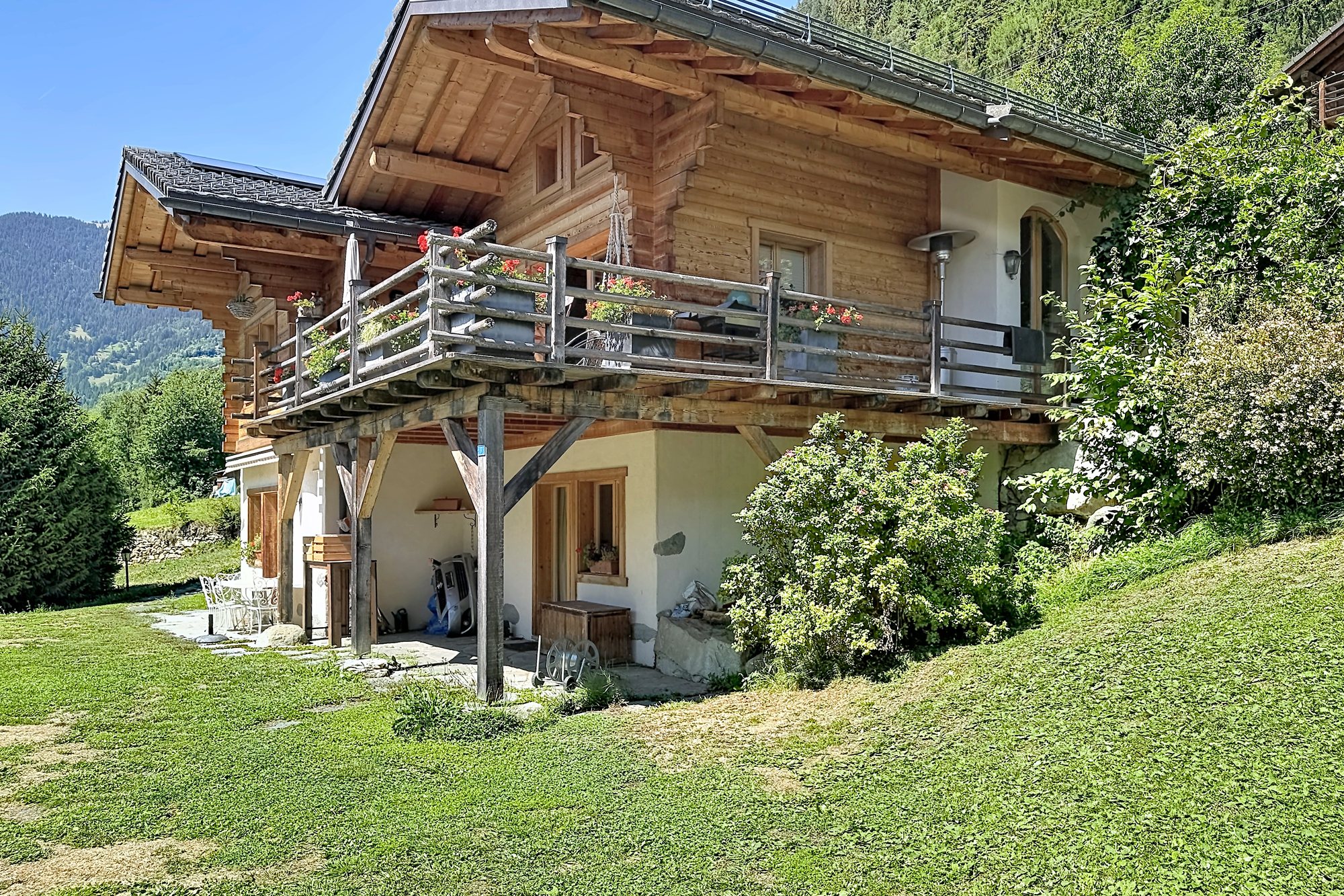 Le chalet de la Tsombe vu du jardin : balcon fleuri filant sur la façade et la vallée de Bagnes en arrière-plan.