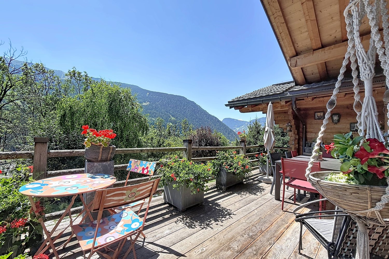 Terrasse en bois avec table bistrot et géraniums, vue plongeante sur la vallée de Bagnes.